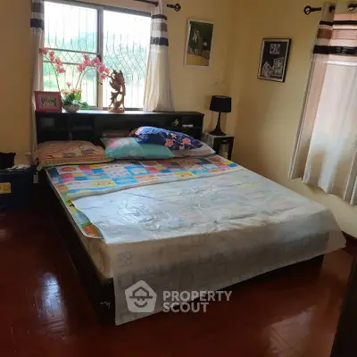 Cozy bedroom with large window and wooden flooring, perfect for relaxation and comfort.