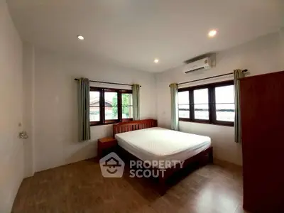 Spacious bedroom with wooden flooring and large windows offering natural light.