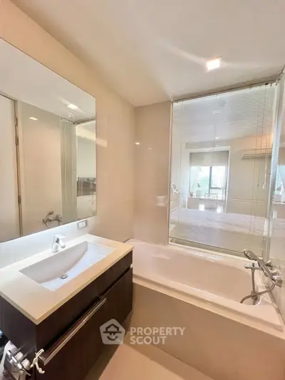 Modern bathroom with sleek fixtures and a bathtub, featuring a large mirror and natural light.