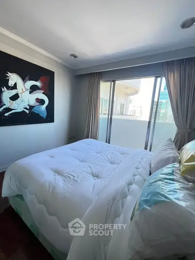 Spacious bedroom with large window and city view, featuring modern art and cozy bedding.