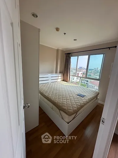 Cozy bedroom with city view and natural light, featuring a comfortable bed and wooden flooring.