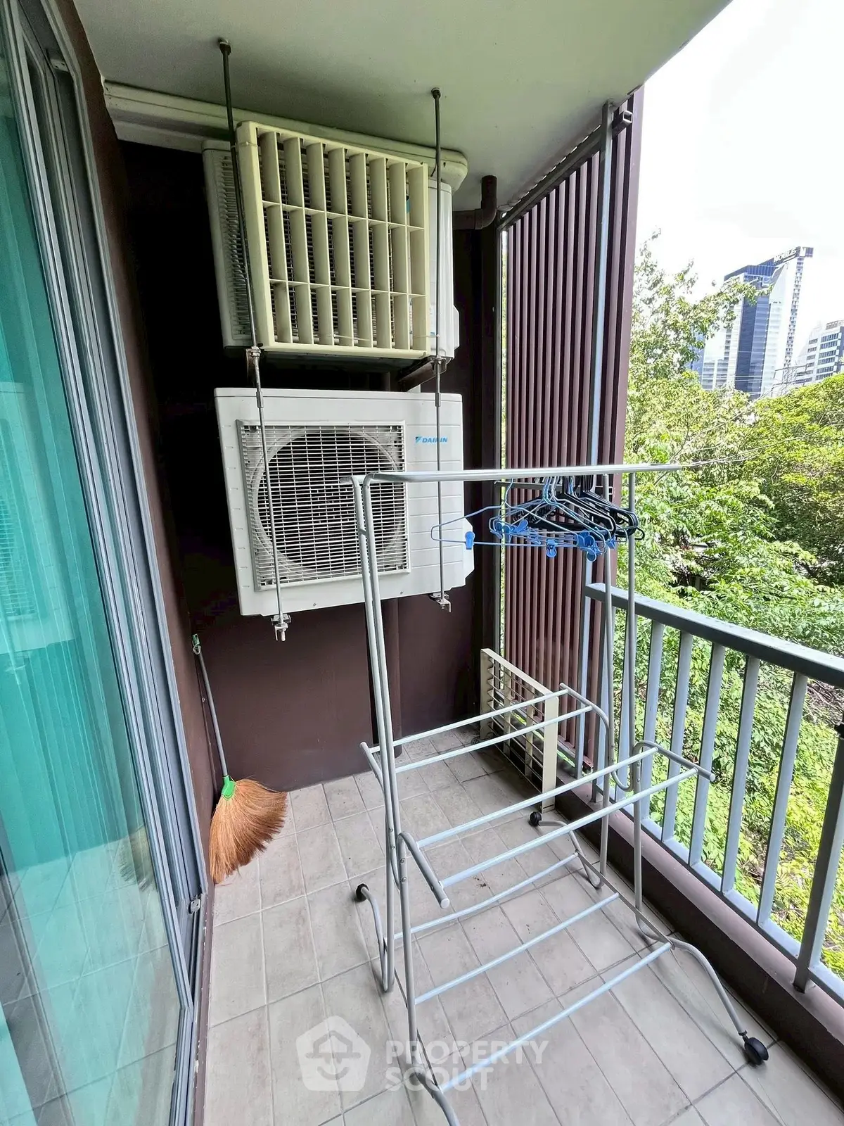 Compact balcony with air conditioning unit and drying rack, overlooking lush greenery.