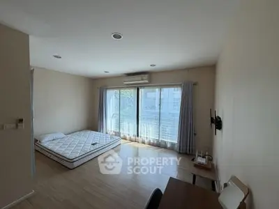 Spacious bedroom with large windows and natural light, featuring a minimalist design and wooden flooring.