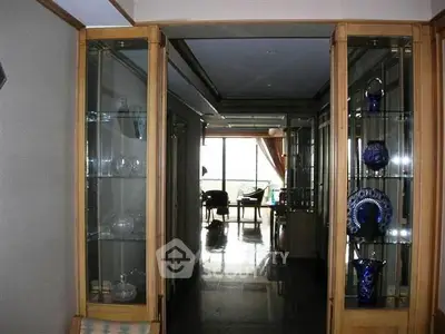 Elegant hallway with glass display cabinets leading to a bright living area with large windows.