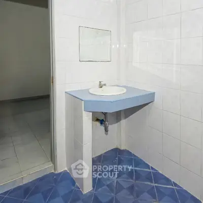 Minimalist bathroom with blue tiled floor and white tiled walls featuring a simple sink and mirror.