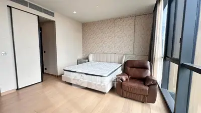 Spacious bedroom with modern design, featuring a comfortable bed and leather armchair by large windows.