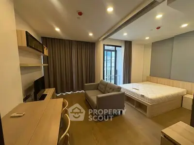 Modern studio apartment with cozy living area and bed, featuring wooden flooring and large windows.