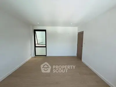 Spacious empty room with wooden flooring and large window, perfect for customization.
