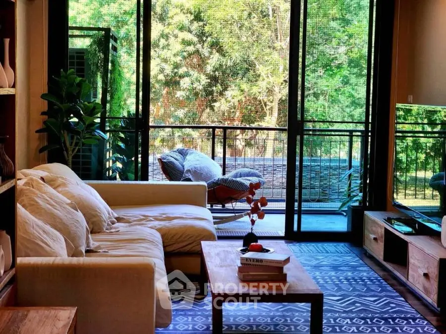 Spacious living room with large windows opening to a lush balcony view, featuring cozy seating and modern decor.