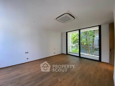 Spacious modern living room with wooden flooring and large windows overlooking greenery.