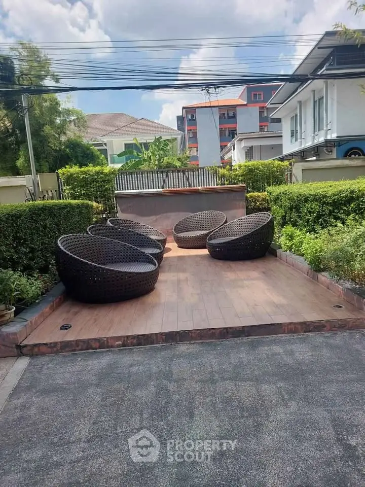 Charming outdoor seating area with modern wicker chairs in a lush garden setting, perfect for relaxation.