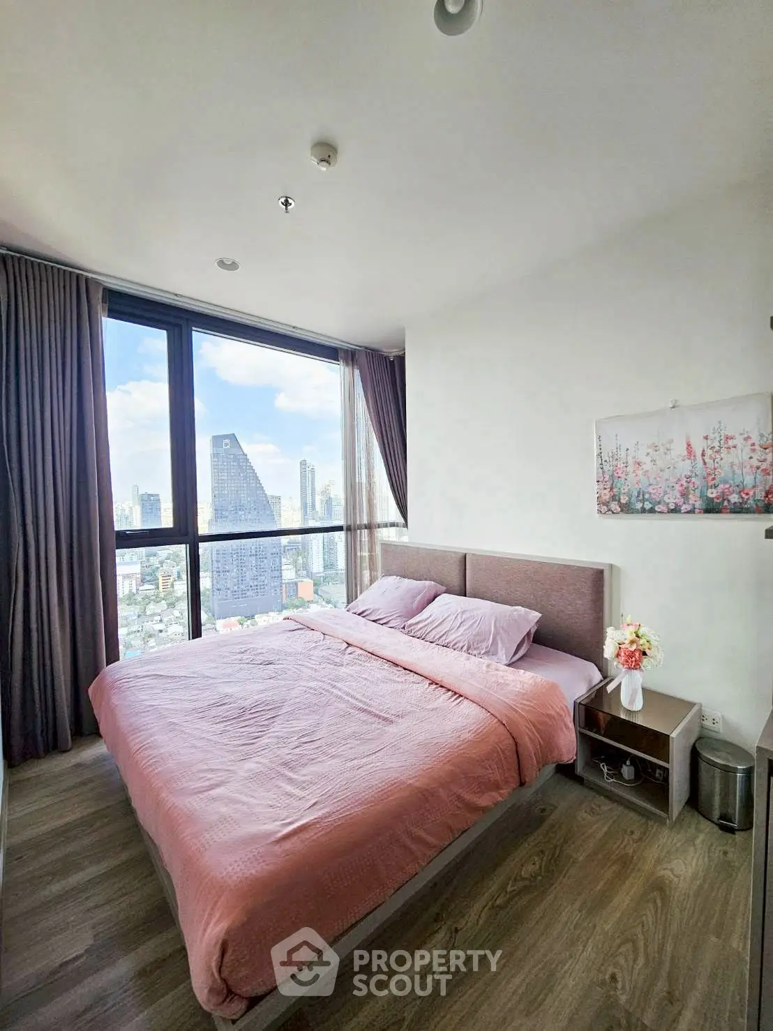 Modern bedroom with stunning city view and cozy decor in high-rise apartment.