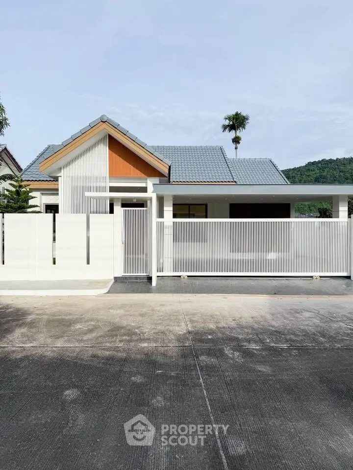 Modern single-story house with sleek white fence and mountain backdrop, perfect for serene living.