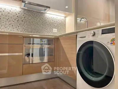 Modern kitchen with built-in oven and washing machine, featuring sleek cabinetry and mosaic backsplash.