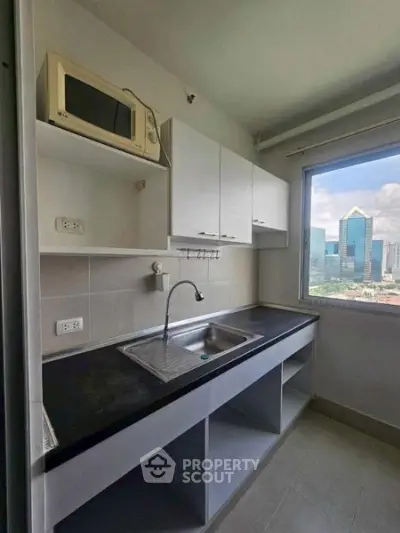 Compact kitchen with city view, featuring modern cabinetry and microwave, ideal for urban living.