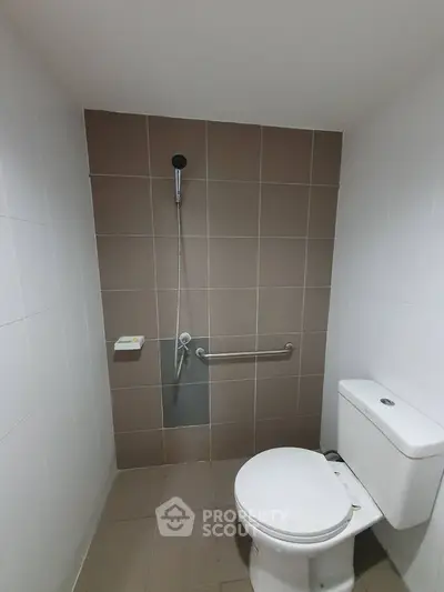 Modern bathroom with tiled walls and toilet, featuring a handheld shower.