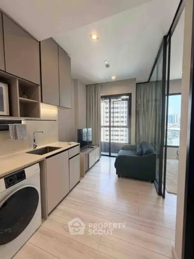 Modern apartment interior with open kitchen and living area, featuring a washing machine and city view.