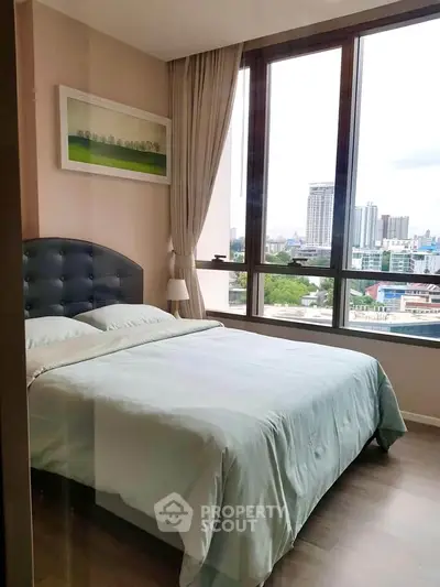 Modern bedroom with large windows offering city views, featuring a cozy bed and elegant decor.