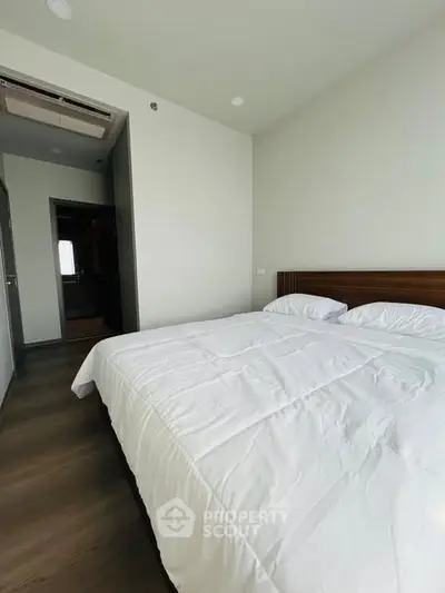 Spacious modern bedroom with cozy white bedding and wooden accents.
