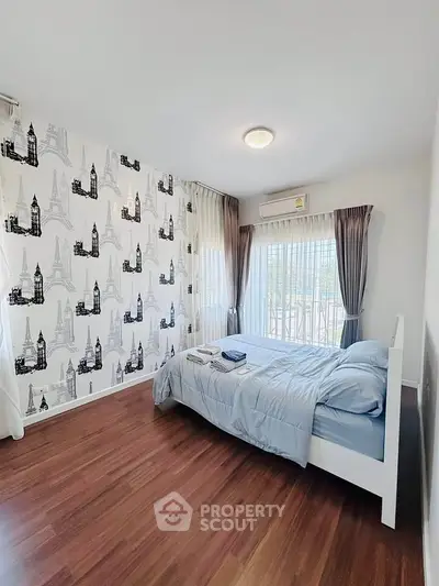 Charming bedroom with elegant wallpaper and large windows offering natural light.