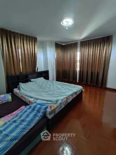Spacious bedroom with large windows and elegant curtains, featuring a cozy bed and polished wooden floor.