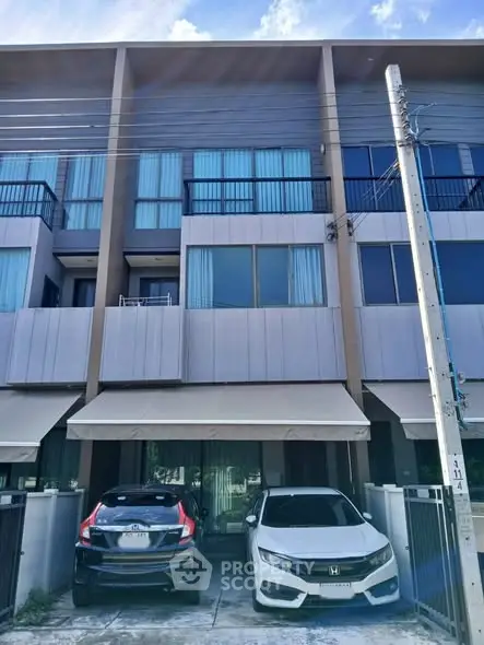 Modern townhouse exterior with two parked cars and large windows.