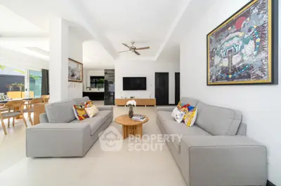 Spacious living room with modern grey sofas, pristine white floors, and an open layout leading to a dining area, accentuated by a vibrant wall art.