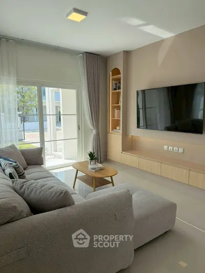 Modern living room with large sofa, wall-mounted TV, and natural light.