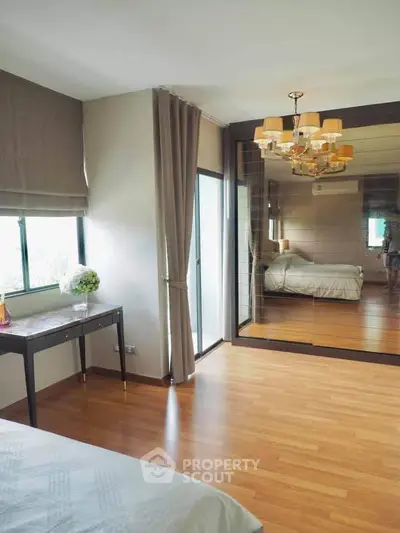 Spacious bedroom with elegant chandelier and mirrored wardrobe, featuring wooden flooring and natural light.