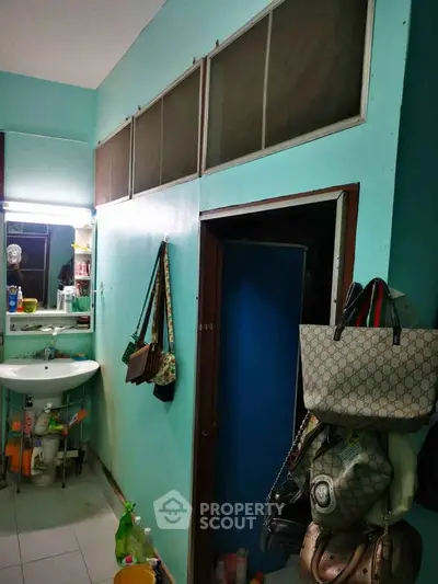 Compact bathroom with sink and storage, vibrant teal walls, and practical hanging space.
