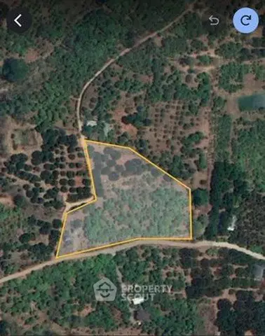 Aerial view of a large plot of land outlined in yellow, surrounded by lush greenery.