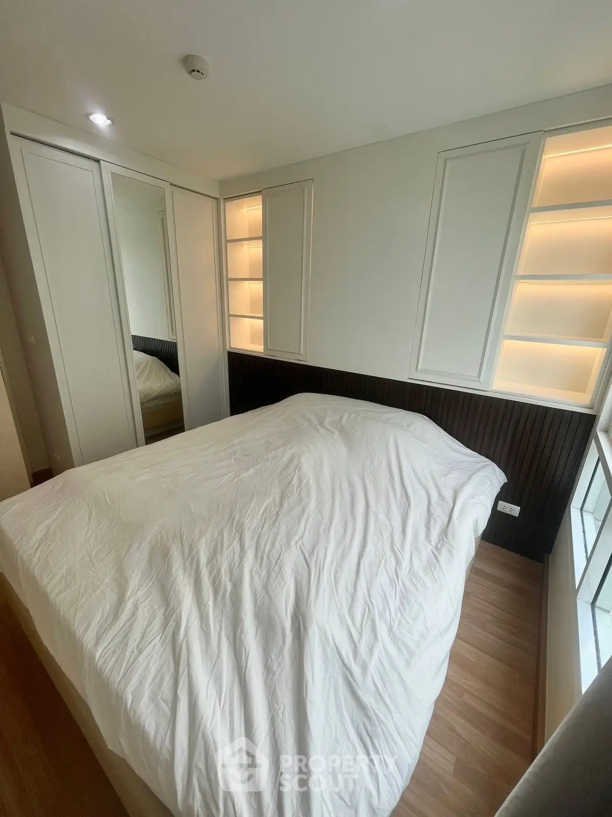 Cozy bedroom with modern design and built-in lighting, featuring a comfortable bed and mirrored wardrobe.