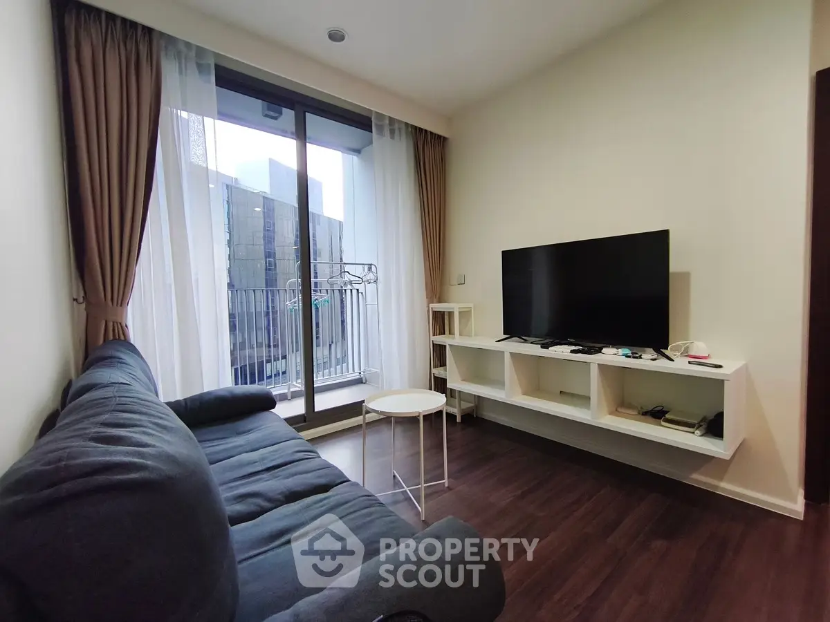 Modern living room with large window and balcony access, featuring a sleek TV setup and comfortable seating.