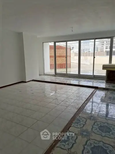 Spacious living room with large windows and tiled flooring, offering ample natural light and outdoor access.