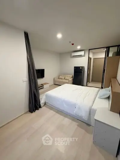 Modern bedroom with cozy bed, TV, and mini fridge in a stylish apartment.