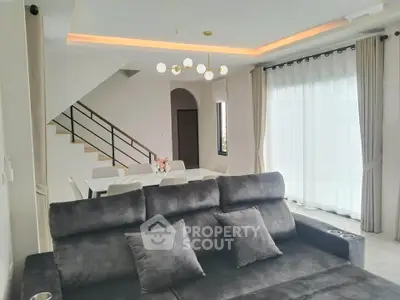 Modern living room with stylish sofa and elegant dining area, featuring large windows and contemporary lighting.