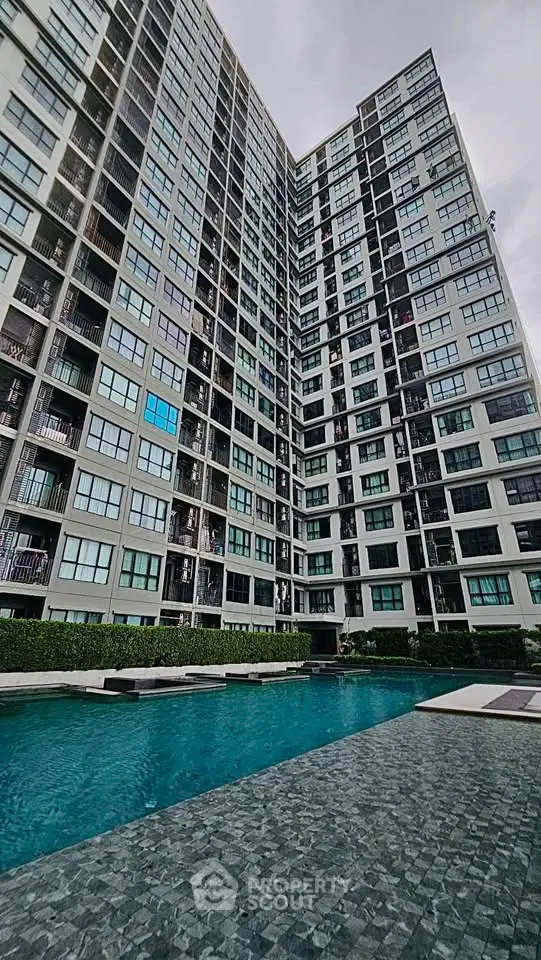 Modern high-rise building with poolside view and lush greenery