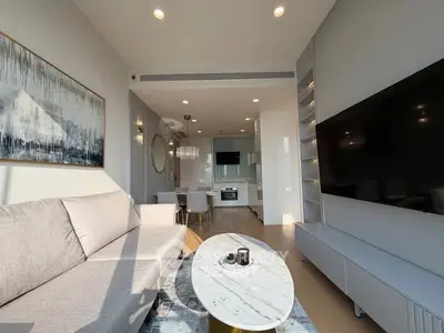 Modern living room with sleek design and large TV, open to kitchen area.