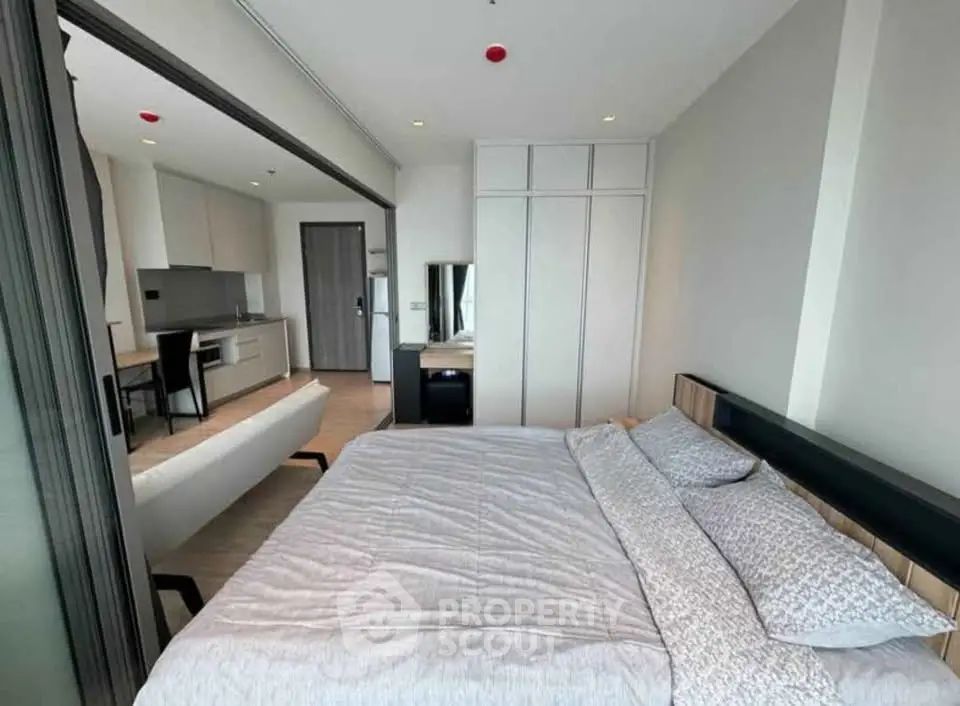 Modern bedroom with sliding doors and open kitchen layout in a stylish apartment.