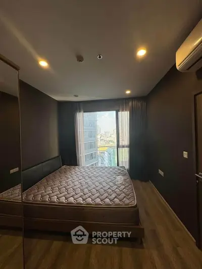 Modern bedroom with city view, featuring a large window, wooden flooring, and air conditioning.