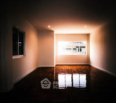 Spacious empty living room with polished wooden floors and large windows.