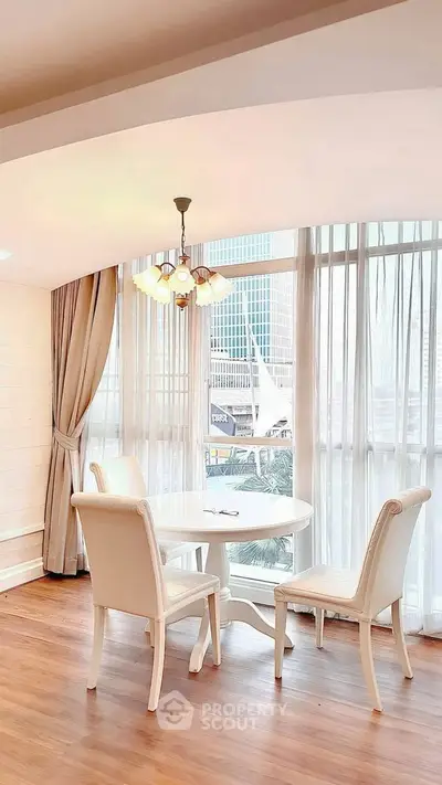 Elegant dining area with natural light and city view, featuring stylish white furniture and wooden flooring.