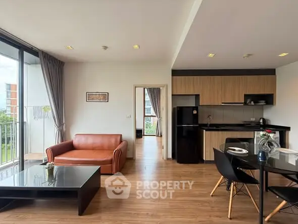 Modern open-plan living room with kitchen, featuring sleek furniture and large windows.