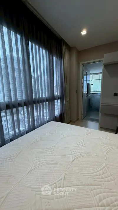 Spacious bedroom with large windows offering city views, connected to a modern bathroom.