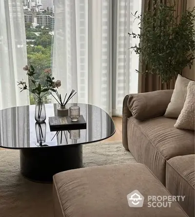 Elegant living room with plush sofa and modern glass coffee table, complemented by sheer curtains and a serene city view, exuding sophistication and comfort.