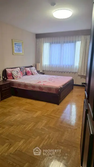 Spacious bedroom with elegant wooden flooring and large window for natural light.