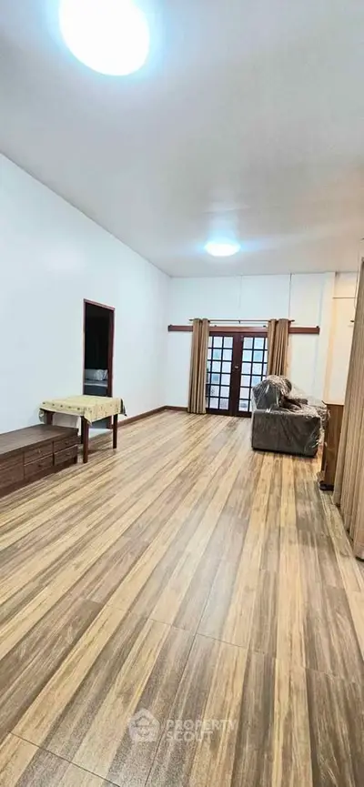 Spacious living room with wooden flooring and large windows for natural light.