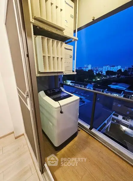 Compact balcony with washing machine and city view at dusk