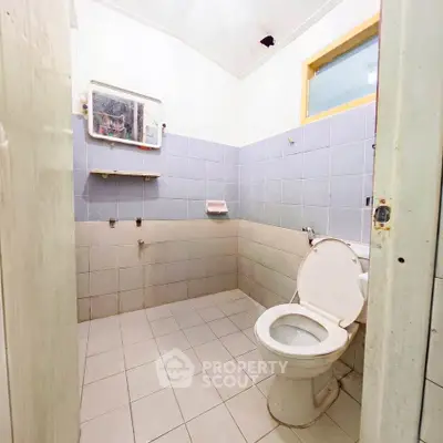 Spacious bathroom with tiled walls and floor, featuring a toilet and mirror.