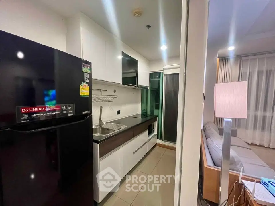 Modern kitchen with sleek cabinetry and adjacent cozy living area in a stylish apartment.